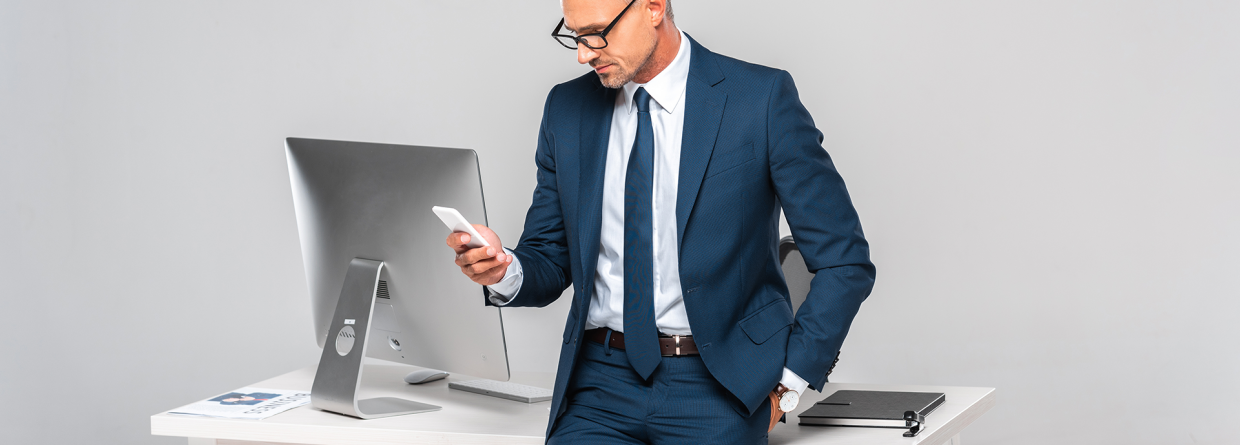 Zakenman leunt tegen bureau aan met een telefoon in zijn hand