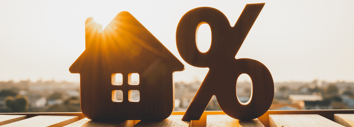 Houten afbeelding van een rentepercentage en een huis op houten planken met de zon op de achtergrond