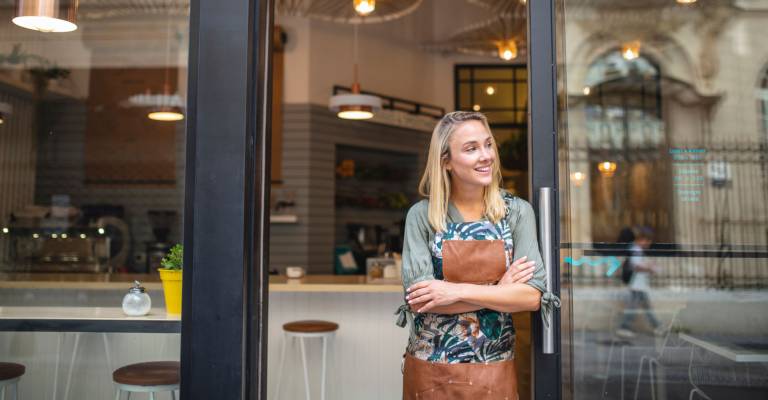 Jonge cafe eigenaar staat met haar armen gekruist bij de voordeur